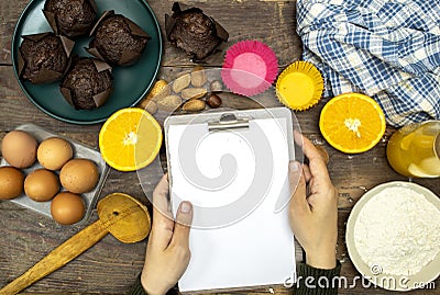 Glass bottle of fresh orange juice with fresh fruits and almond, hazelnuts and homemade chocolate muffins and flour, hands woman h Stock Photo