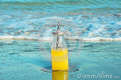 Glass bottle with fresh tropical fruits juice with straw standing on beach sand shore blue turquoise foamy sea waves Stock Photo