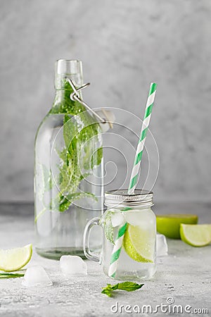 Glass Bottle and lemonade jar with cold lemonade with fresh mint leaves and lime with ice cubes on grey concrete background Stock Photo