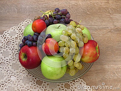 A glass bowl of fresh organic autumn fruit on crochet table cloth and oak wood table background. Stock Photo