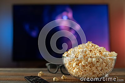 A glass bowl of popcorn, 3d glasses and remote control in the background the TV works. Evening cozy watching a movie or TV series Stock Photo