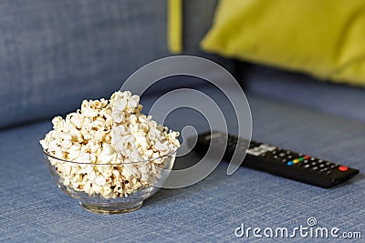 A glass bowl of popcorn and remote control. Evening cozy watching a movie or TV series at Home Stock Photo