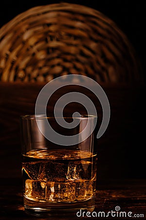Glass chilled whiskey with ice cubes on wooden background in cellar Stock Photo