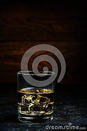 Glass chilled whiskey with ice cubes on wooden background in cellar Stock Photo
