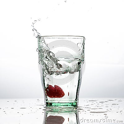 In the glass with clean and transparent water, falls fresh strawberries, splashes water. Stock Photo