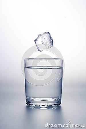 Glass of clear water with an ice cube falling above Stock Photo