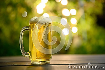 A glass of cold beer with a foam on top Placed on a table in the garden Stock Photo