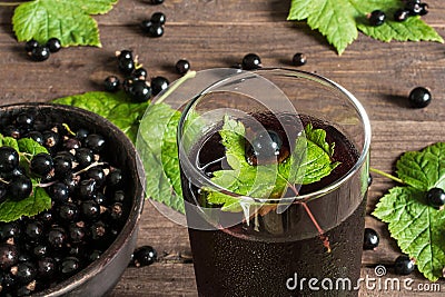 glass of cold black currant juice on wooden table with ripe berries in pottery bowl Stock Photo