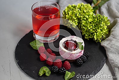 A glass with a compote of berries, next to a plate with blackberries, blueberries, raspberries. Stock Photo