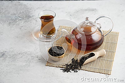 A glass cup of tea with dried loose teas and teapot Stock Photo