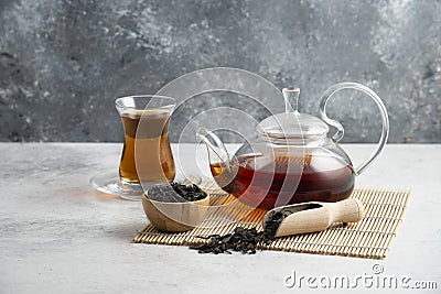 A glass cup of tea with dried loose teas and teapot Stock Photo