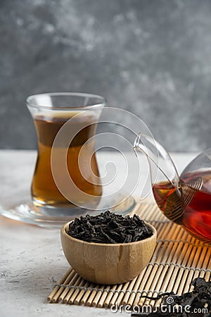 A glass cup of tea with dried loose teas and teapot Stock Photo