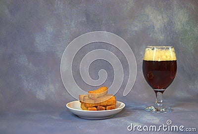 A glass of dark beer with white foam, next to a plate with wheat croutons Stock Photo