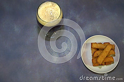 A glass of dark beer with white foam and a plate with wheat croutons on a gray background Stock Photo