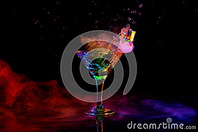 Glass with delicious cocktail with martini against dark background with neon light with smoke. Pouring liquid, splashes Stock Photo