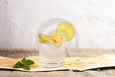 Glass with ginger water on piece of bark on burlap on white textured background. Stock Photo