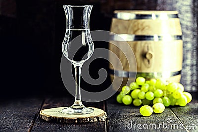 Glass of Grappa on wooden background with old oak barrel, grape-based drink, distilled. Selective focus Stock Photo
