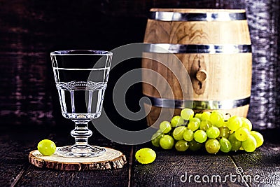Glass of Grappa on wooden background with old oak barrel, grape-based drink, distilled. Selective focus Stock Photo