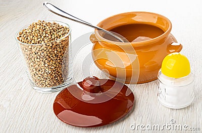 Glass of buckwheat, spoon in ceramic pot, cap, salt shaker on table Stock Photo