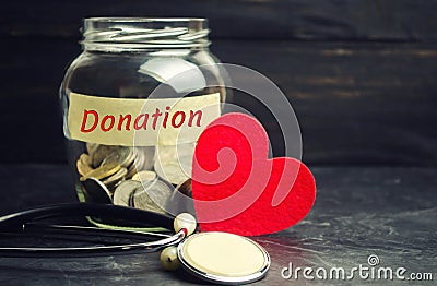 Glass jar with coins, heart and stethoscope and the inscription `Donation`. Medicine concept. blood transfusion, health care. Volu Stock Photo