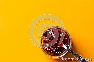 Glass jar with homemade strawberry marmalade with spoon serving on bright yellow background. Making home preserves concept. Summer Stock Photo
