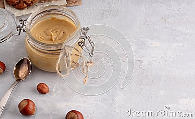 Glass jar with natural nut butter, spoon, healthy cookies, hazelnuts on a light background. Vegetarian traditional breakfast close Stock Photo