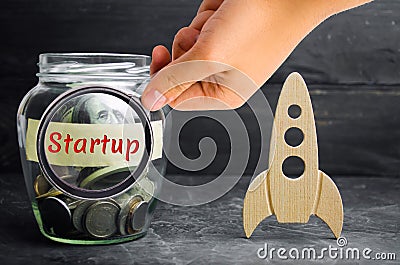 Glass jar, rocket and the word `Startup`. The concept of raising funds for a startup. Charitable contributions to translate ideas Stock Photo