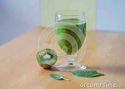 Glass of kiwi smoothie, half of a kiwi and green leaves on a wooden table with blur background Stock Photo