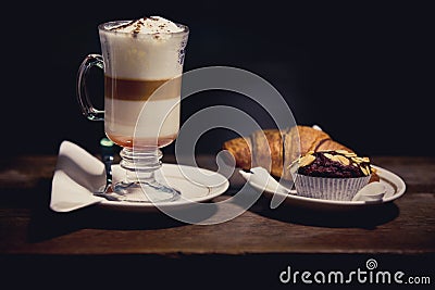 Glass of Latte macchiato with rich milk foam. Hot chocolate and coffee beverage with whipped cream and sweet cupcake and croissant Stock Photo