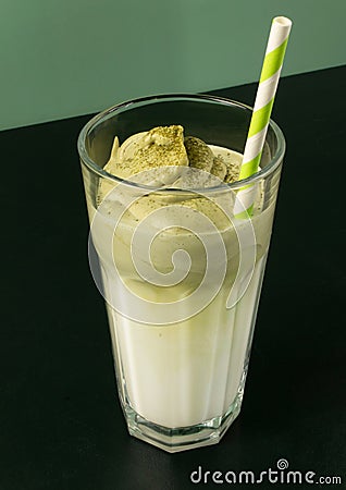 Glass with matcha dalgona and milk with striped paper straw on green background Stock Photo