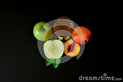 A glass of a mixture of fruit juices and slices of ripe peach and green apple on a black background Stock Photo