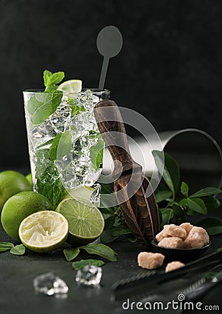 Glass of Mojito cocktail with ice cubes mint and lime on black board with spoon and fresh limes and cane sugar with wooden Stock Photo