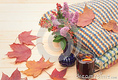 Glass of mulled wine, bouquet made of spirea flowers and barberry branches, stack of warm clothes and autumn maple leaves. Stock Photo