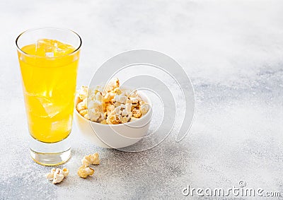 Glass of orange soda drink with ice cubes and white bowl of popcorn snack on stone kitchen table background Stock Photo