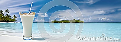 Glass with pina colada cocktail on white sand beach near crystal clear water and vibrant blue sky. Summer seaside vacation concept Stock Photo