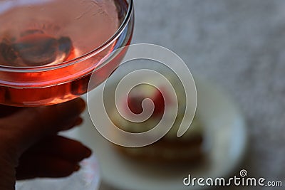 Glass of pink champagne in hand and dessert in the background Stock Photo