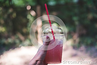 Glass of pink lemonade on hot summer day. Female hand holds plastic glass with straw. Stock Photo