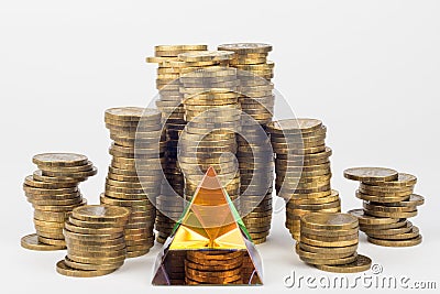 Glass pyramid in the foreground, in the background large stacks of coins Stock Photo