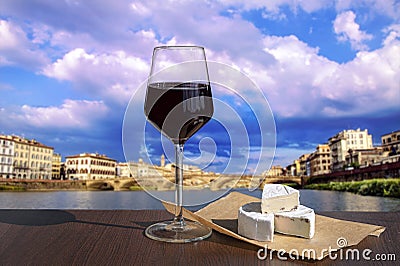 Glass of red wine and brie cheese with view of bridge in Florence during sunset - Ponte alla Carraia, five-arched bridge over Stock Photo