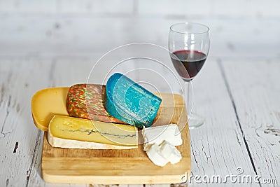 Glass of red wine and variation of cheese on wooden board. Stock Photo