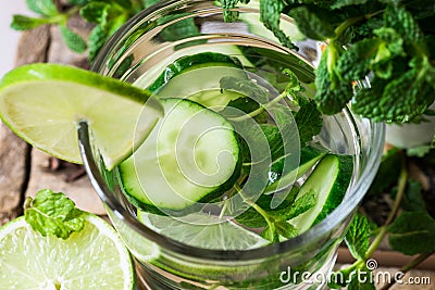Glass with refreshing detox cucumber water with fresh mint and lime on barn wood box, ingredients, spring or summer Stock Photo