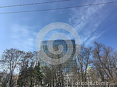 Glass skyscraper on a background of blue sky. Abstract panorama. Tree branches. Editorial Stock Photo