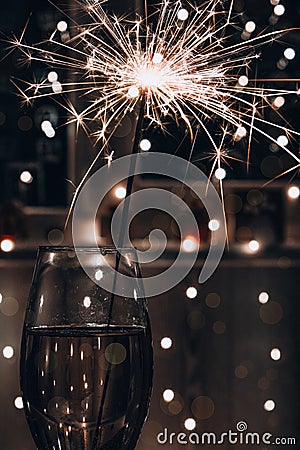 Glass of sparkling wine champagne with sparklers. Dark background with yellow light bokeh. New Year's bengal fire Stock Photo