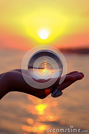 Glass sphere in the palm with an inverted reflection of the sunset on the sea in Turkey in Kizilagac Stock Photo