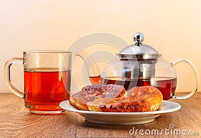 Glass teapot and cup with tea and plate of pancakes on wooden surface on yellow background Stock Photo