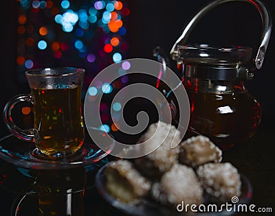 A glass teapot with tea, a glass glass on a saucer with tea and cakes with cream filling in chocolate glaze. Stock Photo