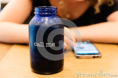 Glass with the Text Call Me on Background of Woman texting on Phone Waiting for answer or Phone Call Stock Photo