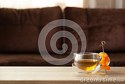 Glass thermo cup with green tea and dried apricots on wooden table against defocused sofa with pillows. Front view. Mock-up Stock Photo