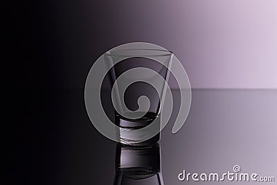 Glass for vodka on glass bar counter, empty shot glass on purple background in nightclub Stock Photo