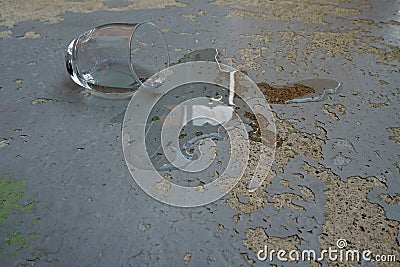 Glass of water overturned or tipped over on the concrete plate with peeling off old paint. Stock Photo